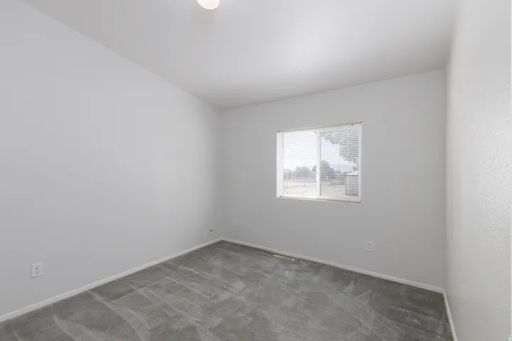 Neutral-toned room featuring a single window with horizontal blinds, light gray wall-to-wall carpeting, white baseboards, and a flush-mount ceiling light fixture
