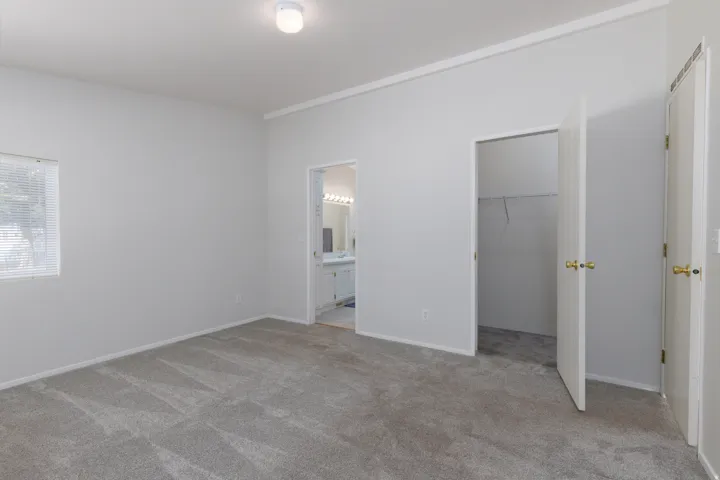 Carpeted room featuring a window with blinds, a ceiling-mounted light fixture, a closet with bi-fold doors, and an entryway to a bathroom with a dual vanity