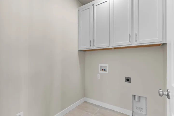 Laundry area featuring shaker-style upper cabinetry with brushed nickel hardware, light-toned wall paint, and tile flooring
