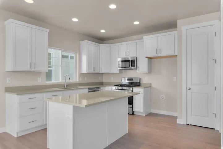 Modern kitchen featuring white cabinetry, light-toned countertops, stainless steel appliances, a central island, and wood-finish flooring