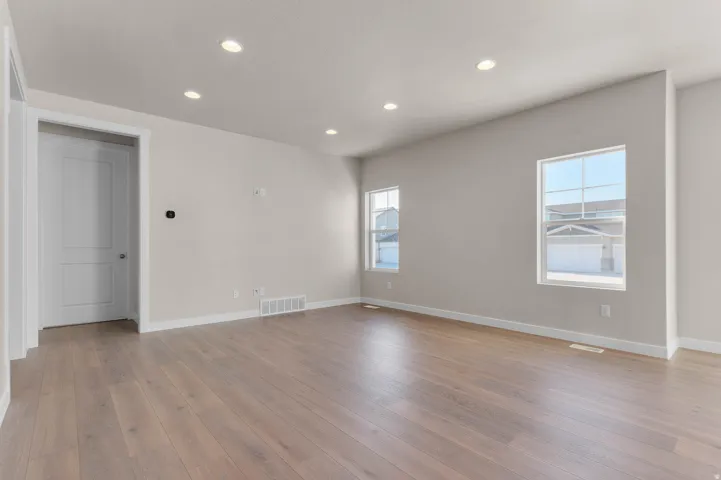 Spacious living area featuring wood-finish flooring, recessed lighting, neutral wall tones, and multiple windows providing natural illumination