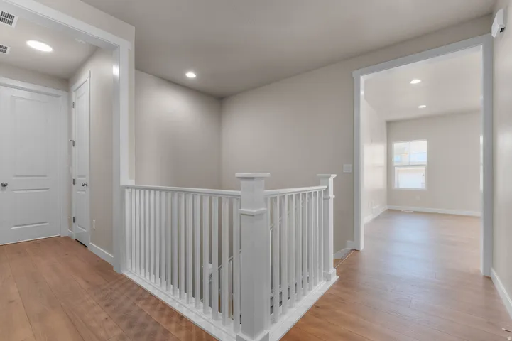 Upper landing with wood-finish flooring, white spindle railing, recessed lighting, and neutral wall tones