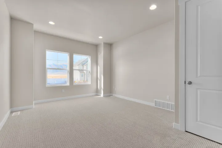 Carpeted room featuring two large windows, recessed ceiling lighting, and a white paneled door