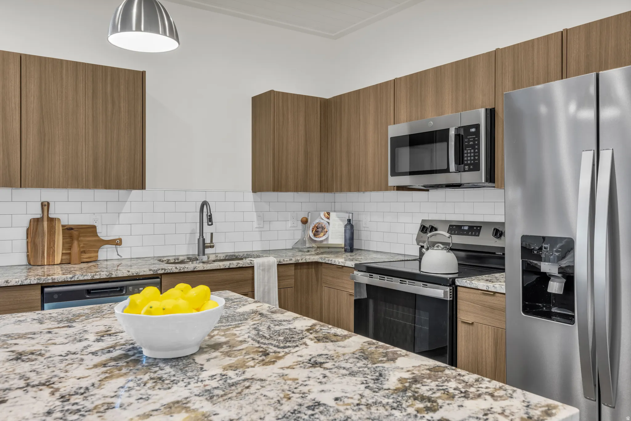 Kitchen featuring wood-finish cabinetry, granite countertops, white subway tile backsplash, and stainless steel appliances