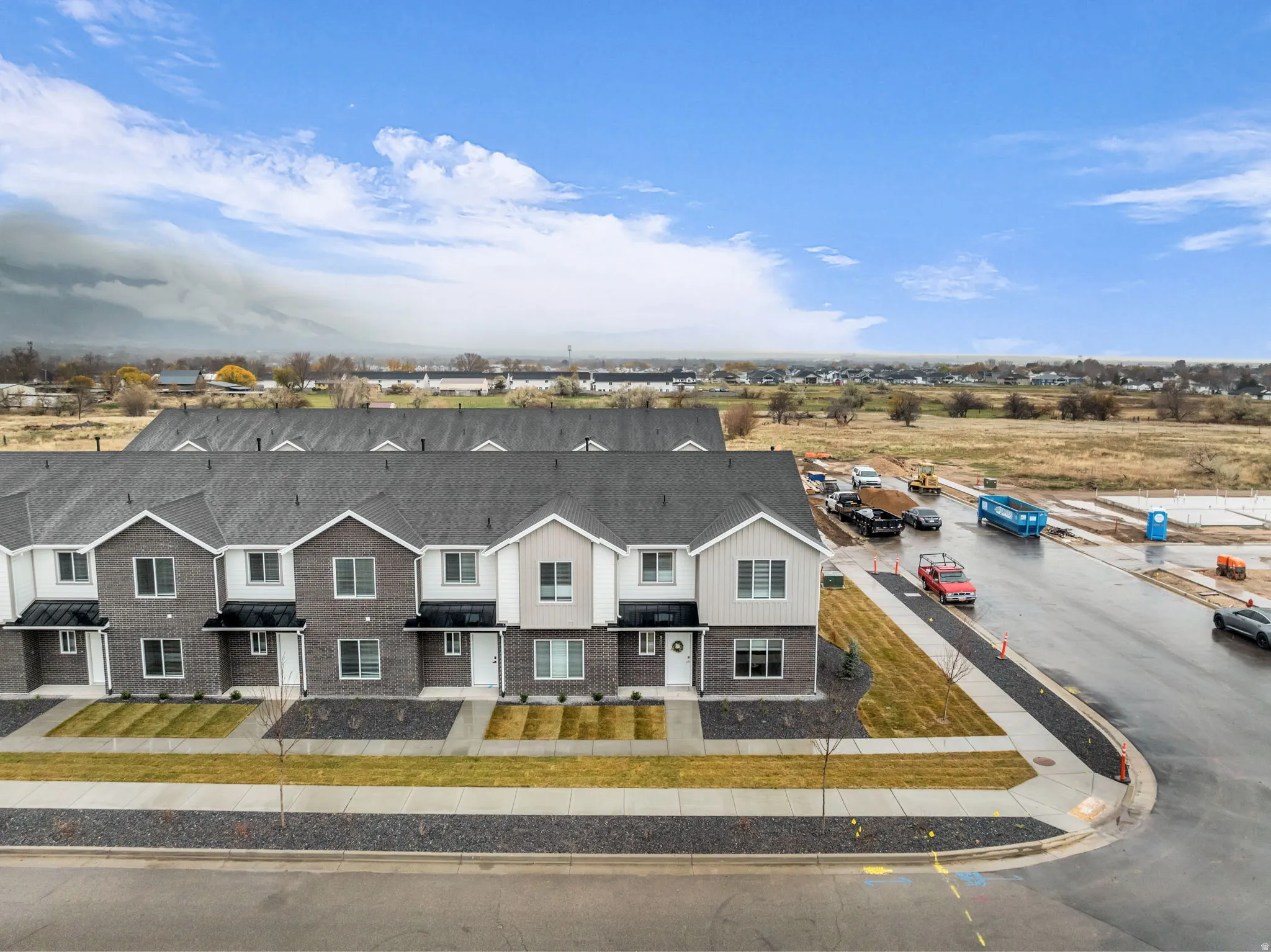 Newly constructed townhomes featuring modern exteriors with brick and siding facades, dark asphalt shingle roofs, and individual front entrances