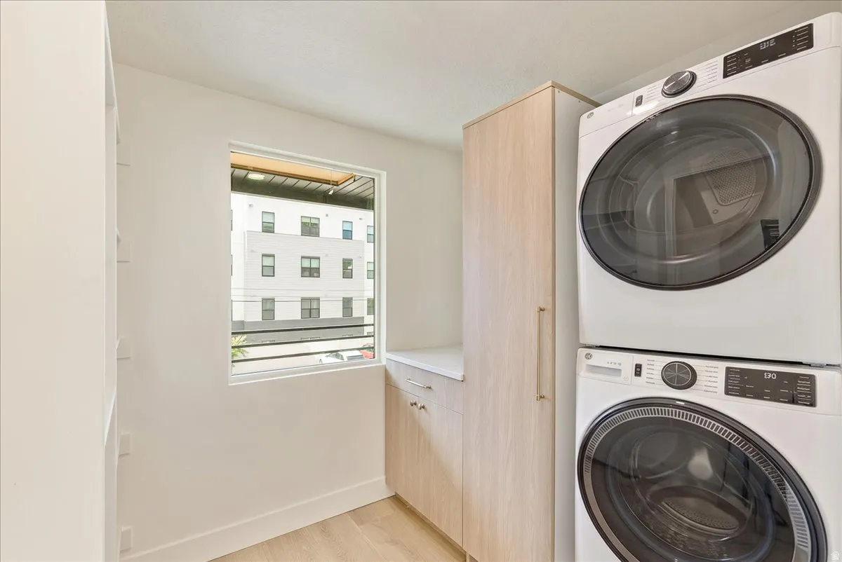 Laundry area with a stacked washer and dryer, wood-finish flooring, and a window