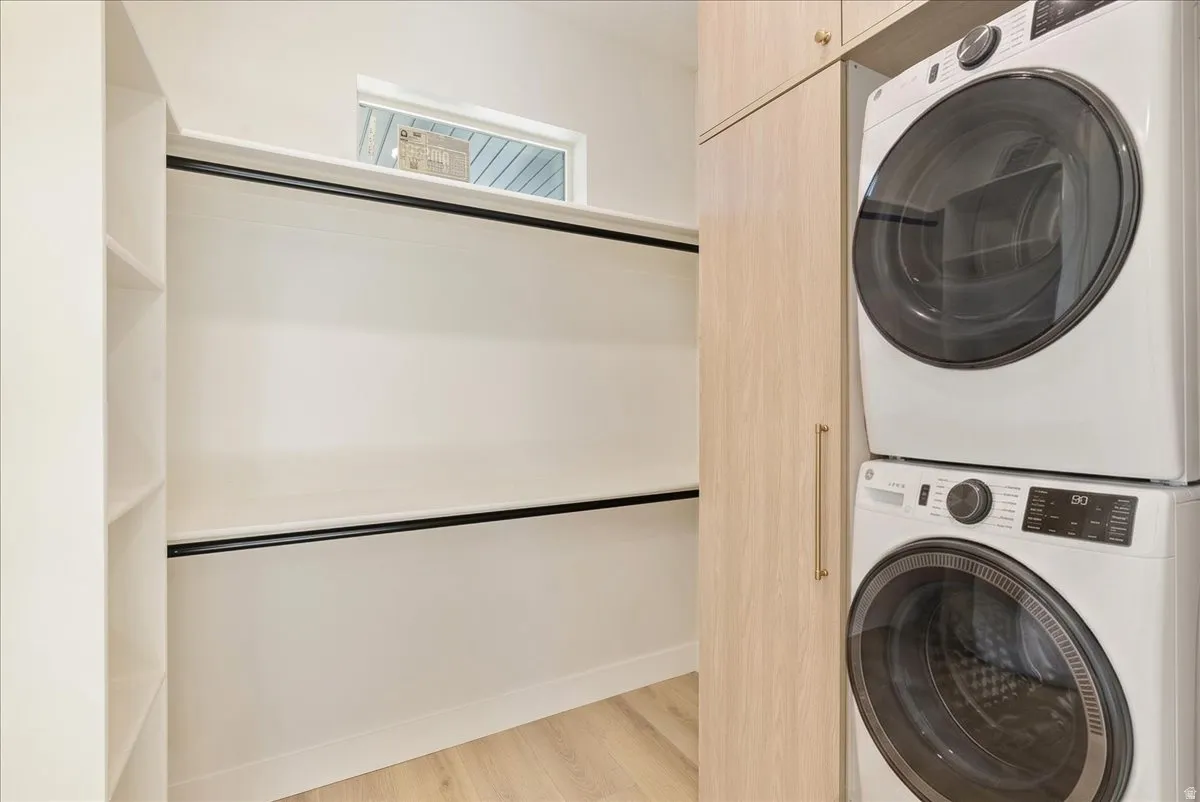 Dedicated laundry area featuring a stacked washer and dryer unit, wood-finish cabinetry, built-in shelving, and light wood-finish flooring