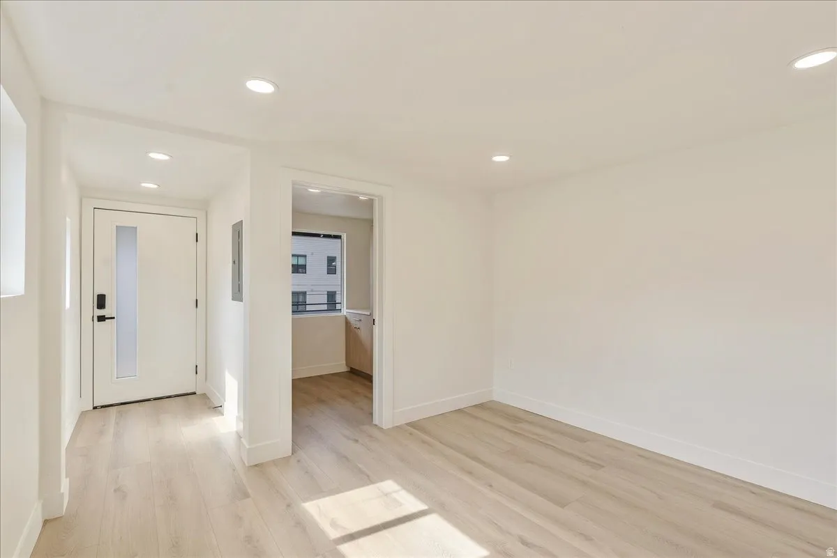 Open-concept interior featuring light wood-finish flooring, recessed lighting, and crisp white walls