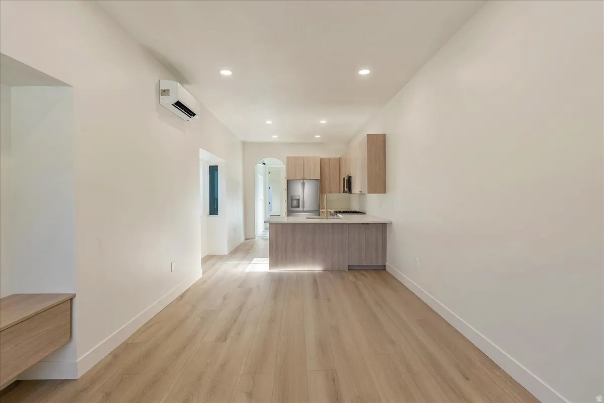 Open-concept living space featuring light wood-finish flooring, recessed lighting, and a modern kitchen with light wood-finish cabinetry, stainless steel appliances, and a central island with countertop seating