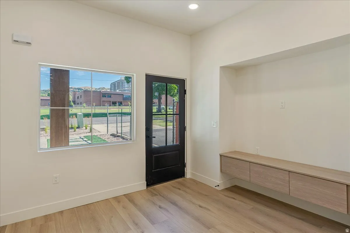 Spacious entryway featuring light wood-finish flooring, a contemporary black door with windowpanes, a large horizontal window, a built-in media niche, and a floating wood-finish cabinet with three drawers