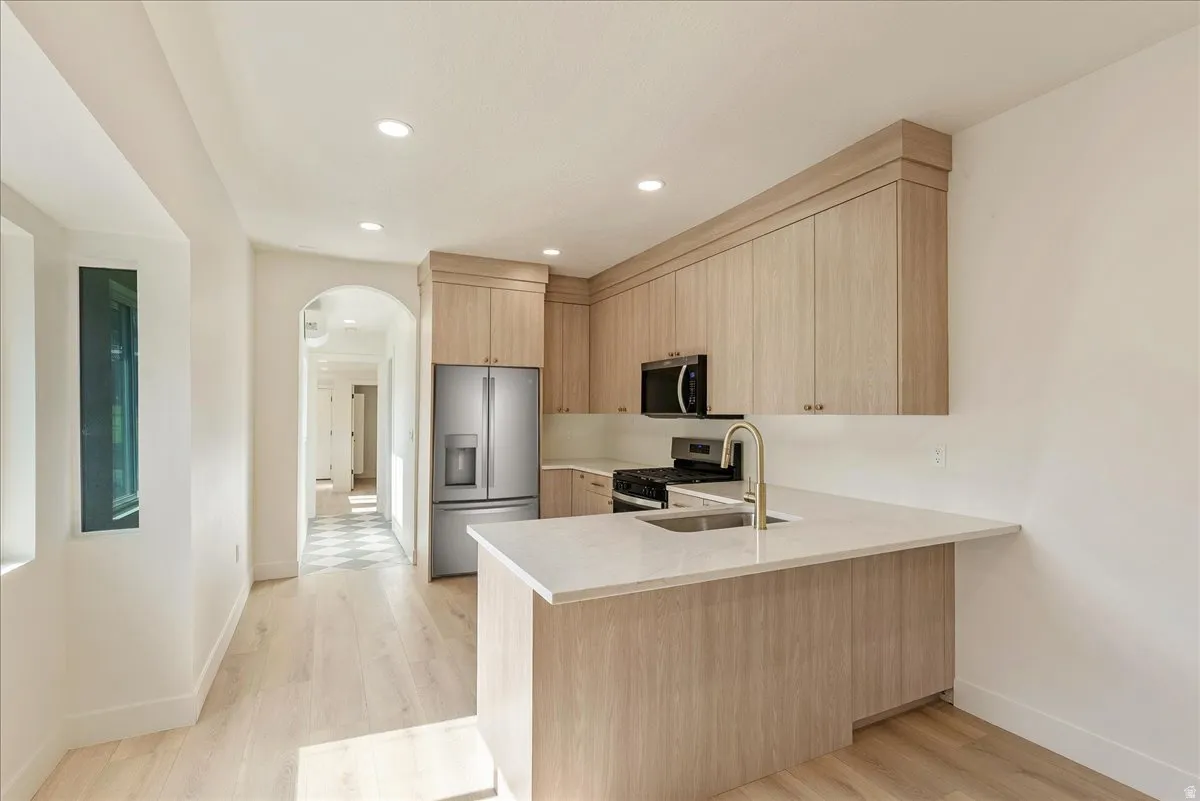 Modern kitchen featuring light wood-finish cabinetry, stainless steel appliances, a white countertop island with seating space, and recessed lighting