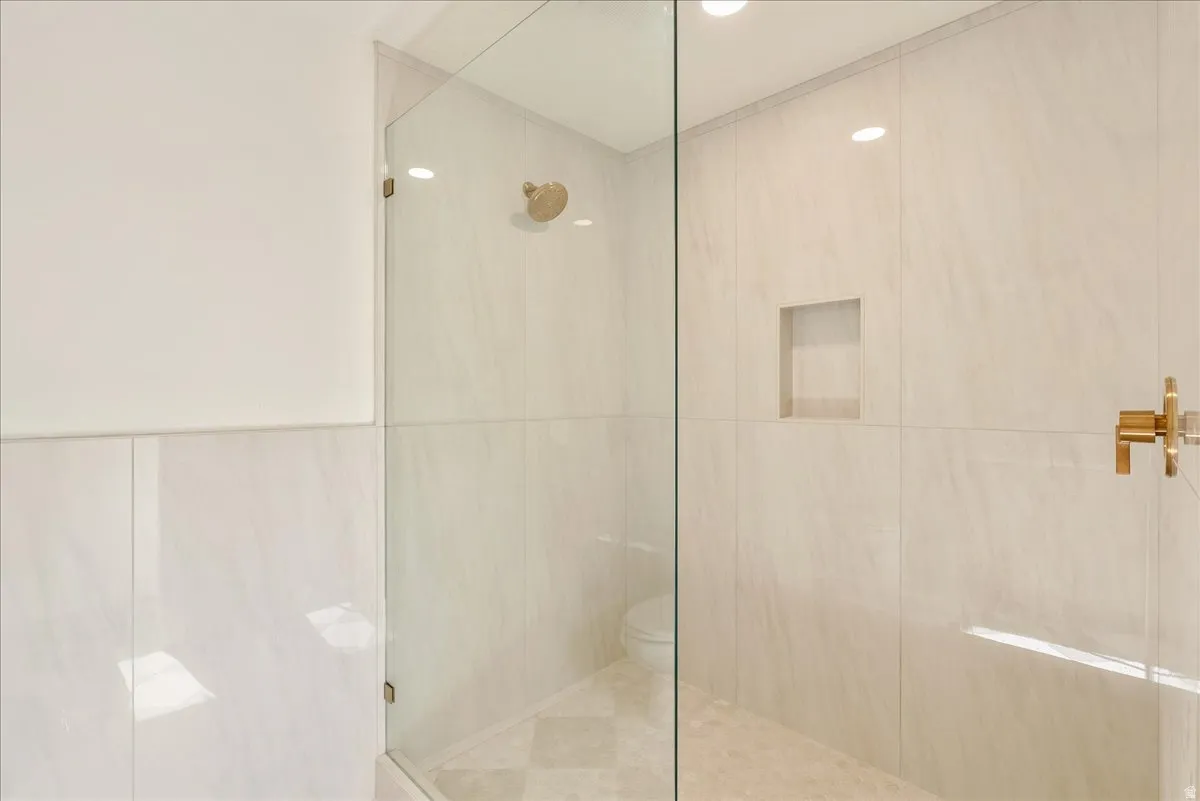 Spacious shower enclosure featuring clear glass panels and brass-finish fixtures, including a rainfall showerhead and control handles