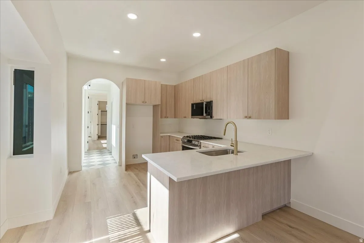 Modern kitchen featuring light wood-finish cabinetry, a central island with a sink, stainless steel appliances, and wood-finish flooring