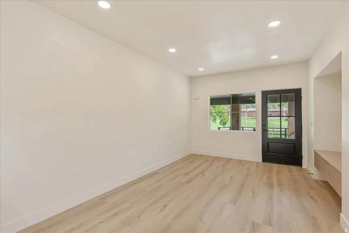 Spacious room featuring light wood-finish flooring, recessed ceiling lighting, a dark-framed glass paneled door, and a horizontal window