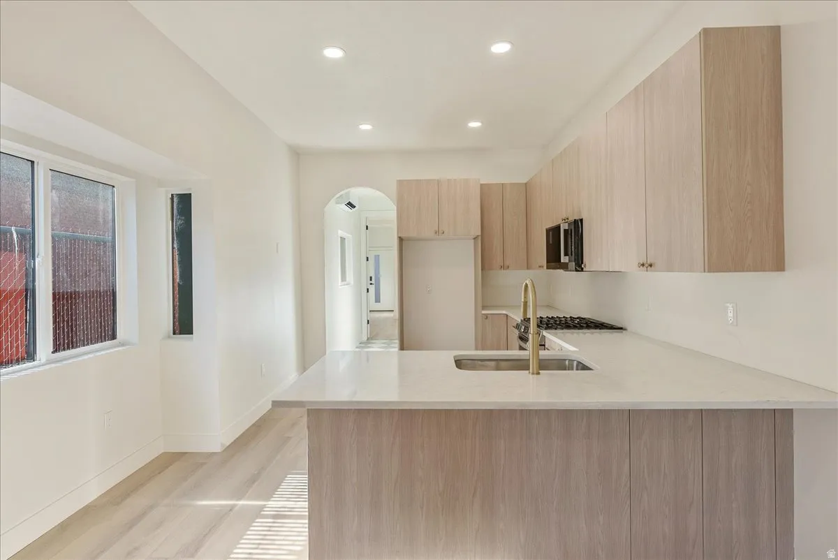 Contemporary kitchen featuring light wood-finish cabinetry, a large center island with a stainless steel sink, a modern gold-tone faucet, and an integrated gas cooktop