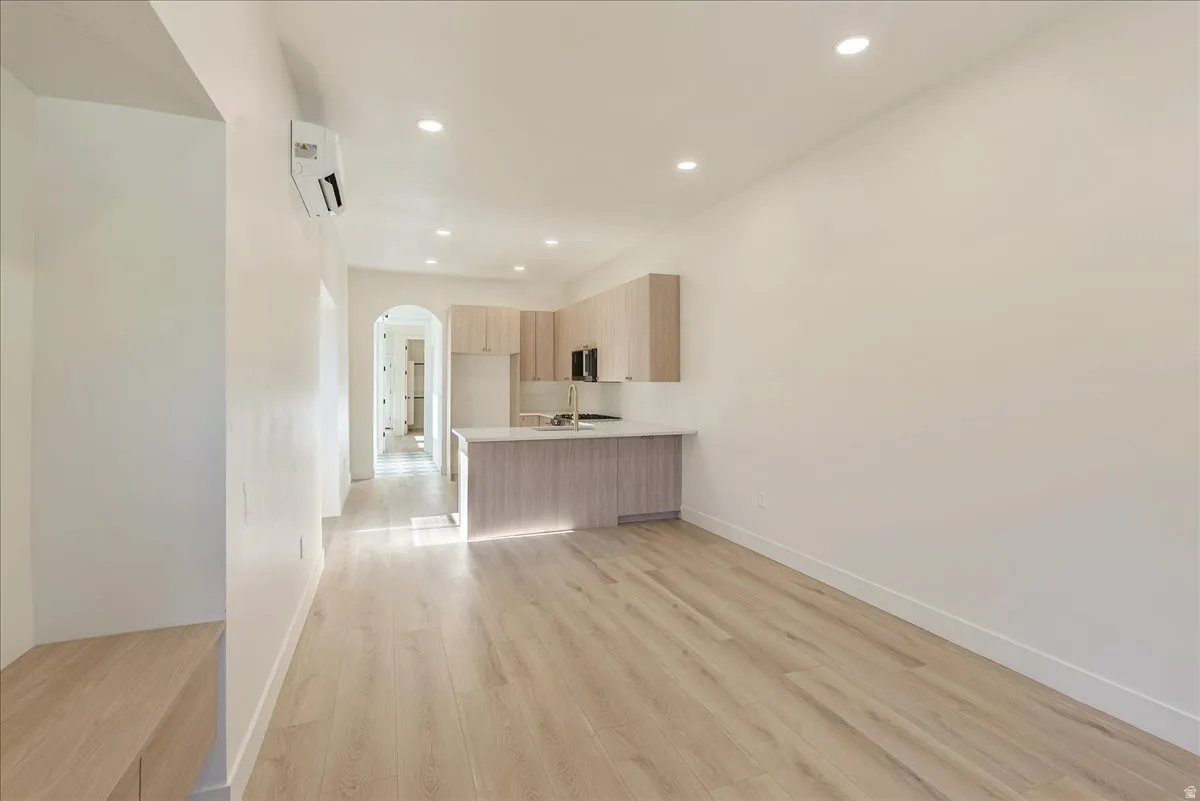 Open-concept living area featuring light wood-finish flooring, recessed lighting, and a modern kitchen