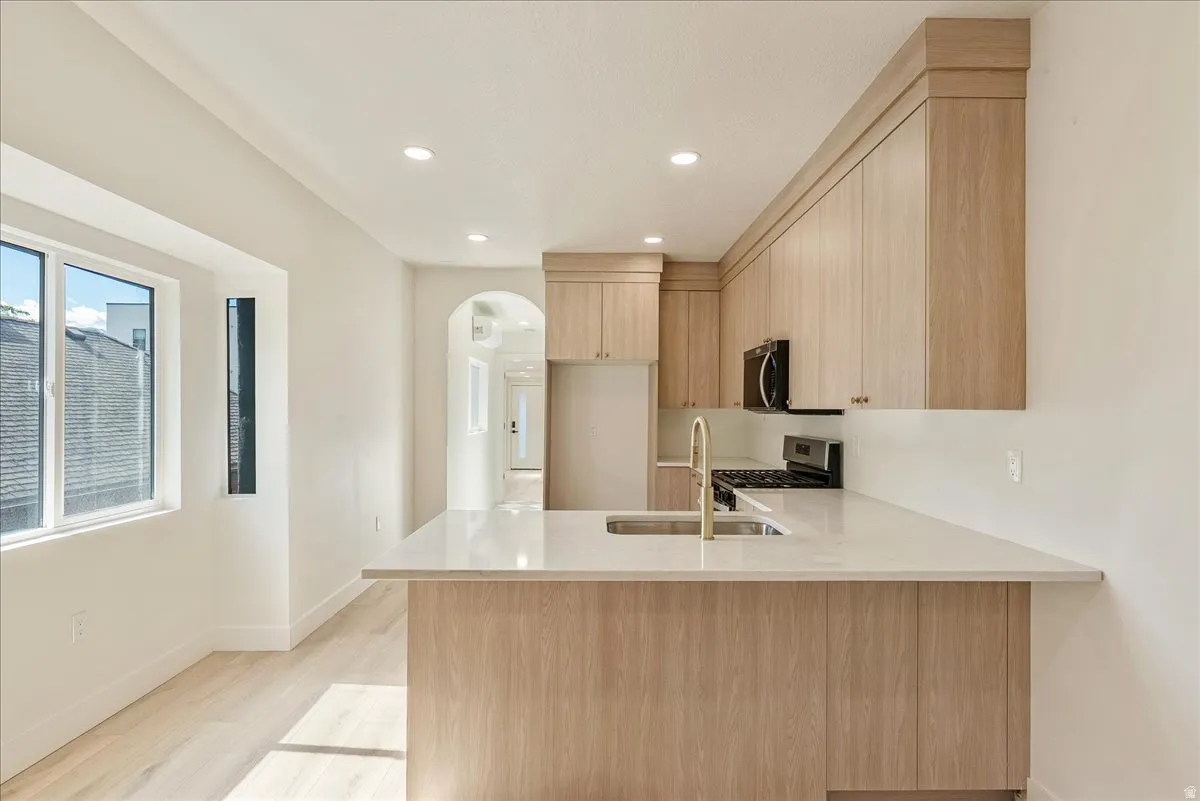 Modern kitchen featuring light wood-finish cabinetry, a large center island with a sink and brass-finish faucet, light-toned countertops, and recessed lighting