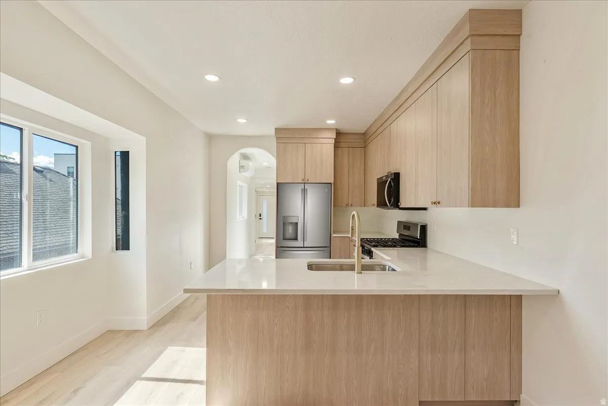 Contemporary kitchen featuring light wood-finish cabinetry, a large center island with an undermount sink and gold-finish faucet, and integrated stainless steel appliances