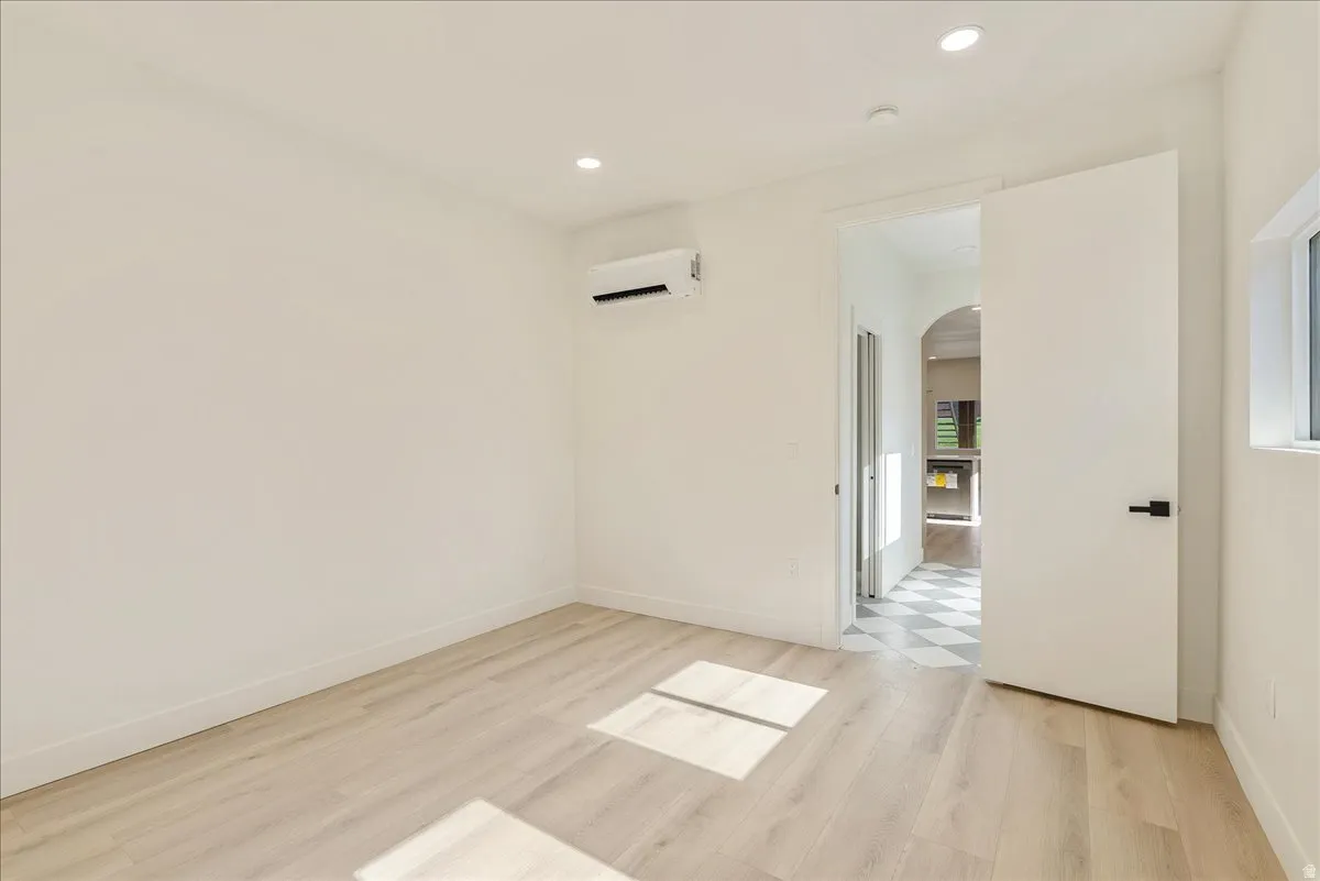 Bright room featuring light wood-finish flooring, recessed lighting, and a wall-mounted mini-split HVAC unit