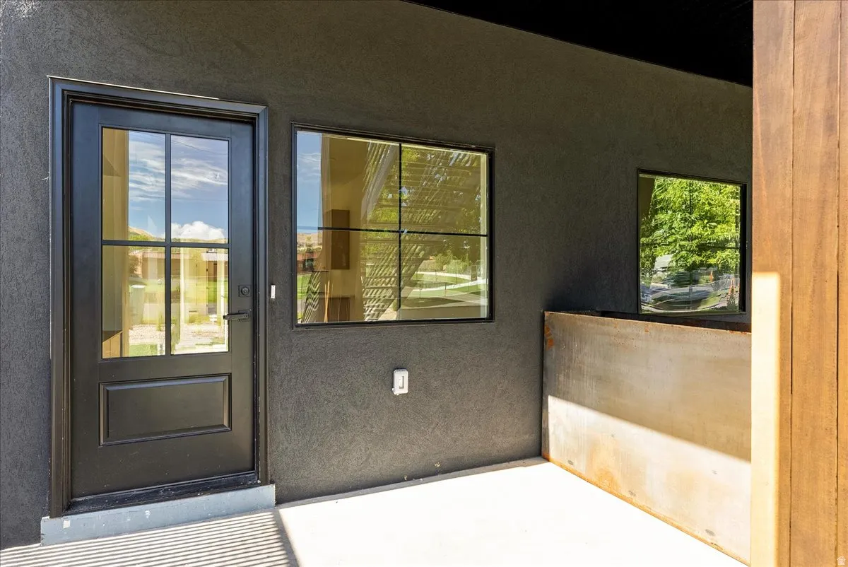 Exterior entrance featuring a black paneled door with glass inserts, complementing black-framed windows, and a concrete patio