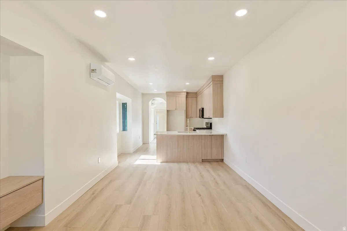 Open-concept living space with light wood-finish flooring, recessed ceiling lighting, and a kitchen featuring light wood cabinetry