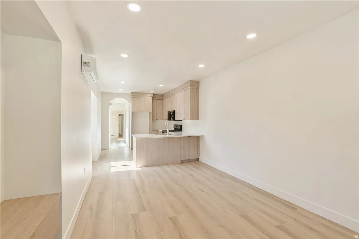 Open-concept living area featuring wood-finish flooring, recessed lighting, and a modern kitchen with light wood-finish cabinetry