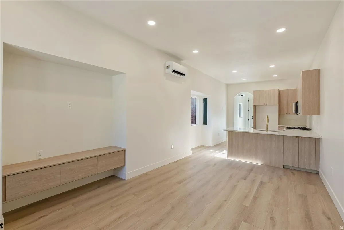 Open-concept living space with light wood-finish flooring, recessed lighting, and a built-in media console