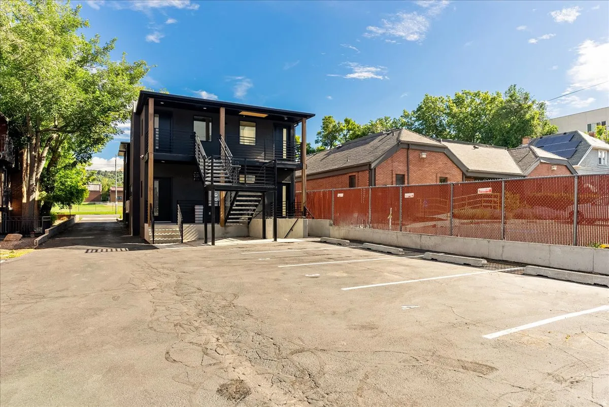 Modern multi-story structure featuring dark siding and prominent exterior staircases, complemented by a substantial paved parking area with marked spaces