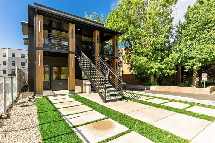 Modern multi-level exterior featuring dark siding, natural wood-finish columns, and a prominent exterior staircase with metal railings