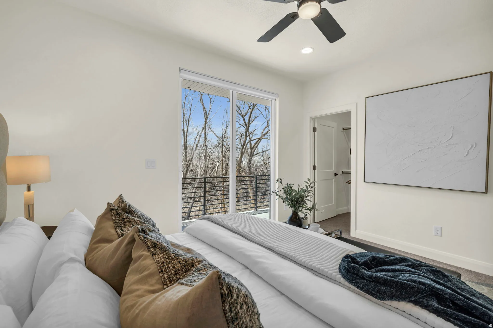 Spacious room featuring floor-to-ceiling sliding glass doors, a private balcony with black metal railings, a ceiling fan with integrated lighting, recessed lighting, and a white paneled door leading to a closet