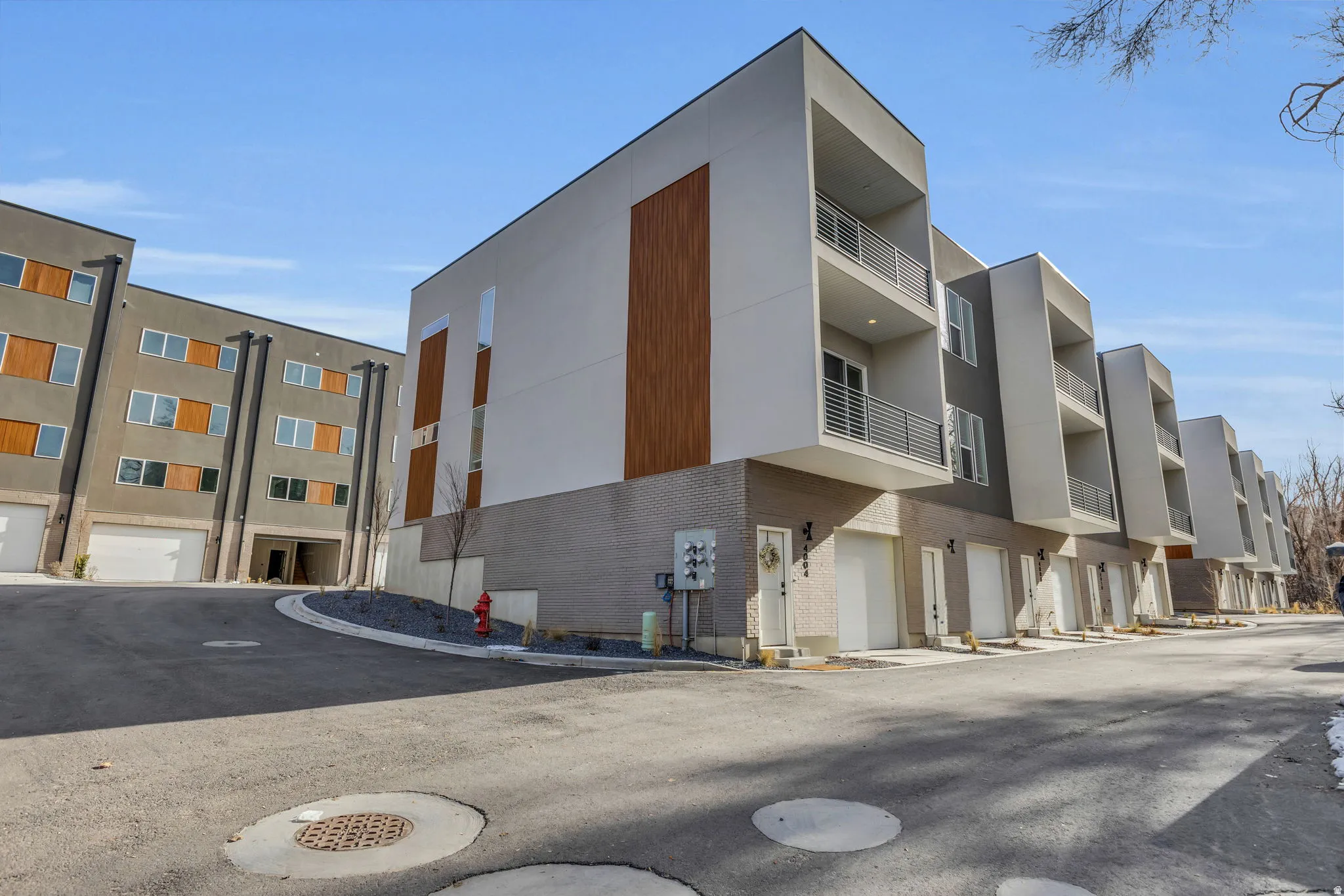 Contemporary multi-level townhome featuring a minimalist exterior design with white stucco, wood-look accents, and gray brickwork