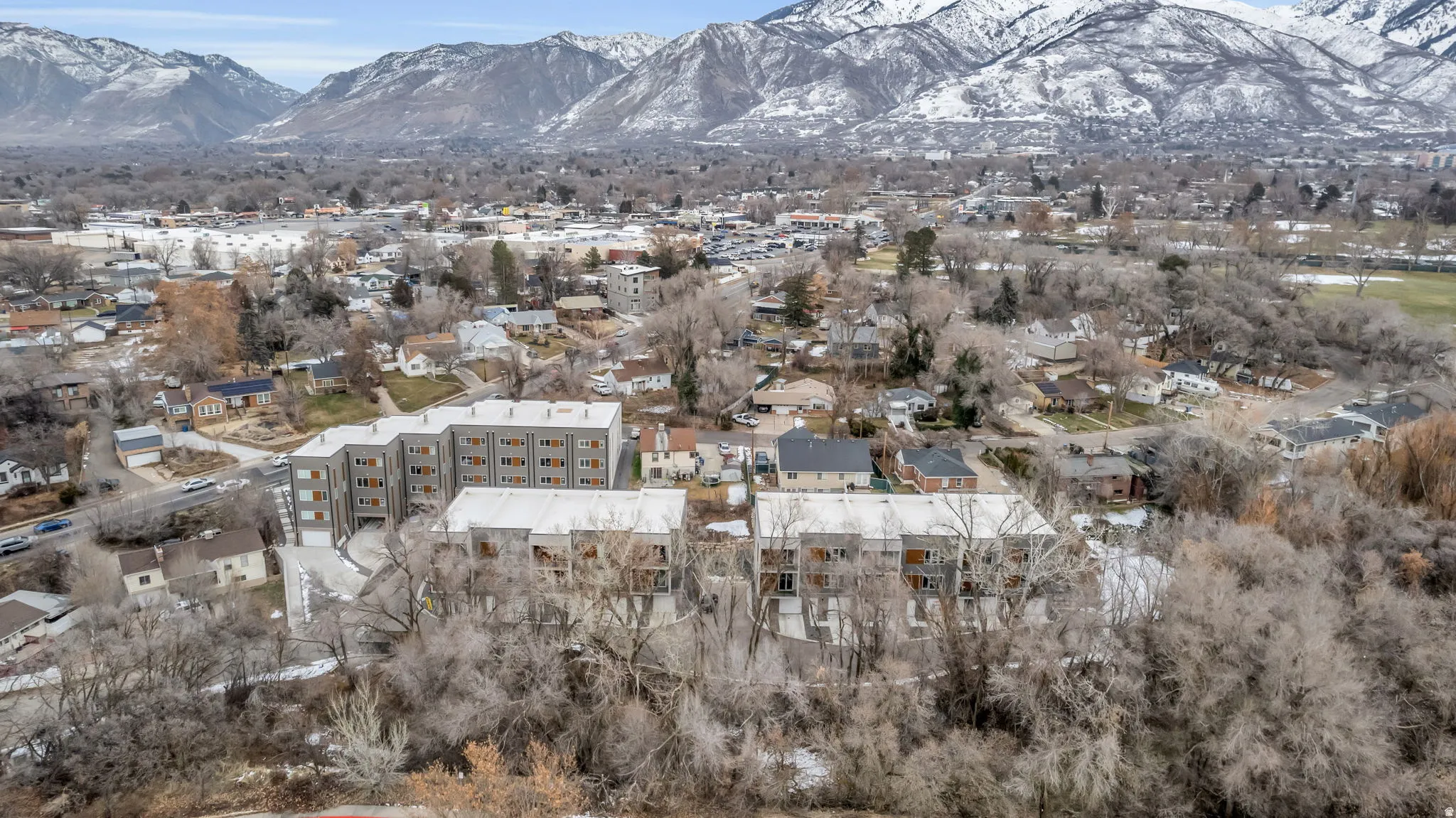 Modern multi-story residential buildings featuring balconies and gray facades, situated within a developed area with extensive tree cover
