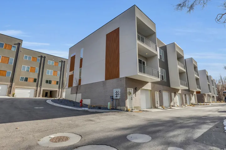 Contemporary multi-level townhome featuring a minimalist exterior design with white stucco, wood-look accents, and gray brickwork