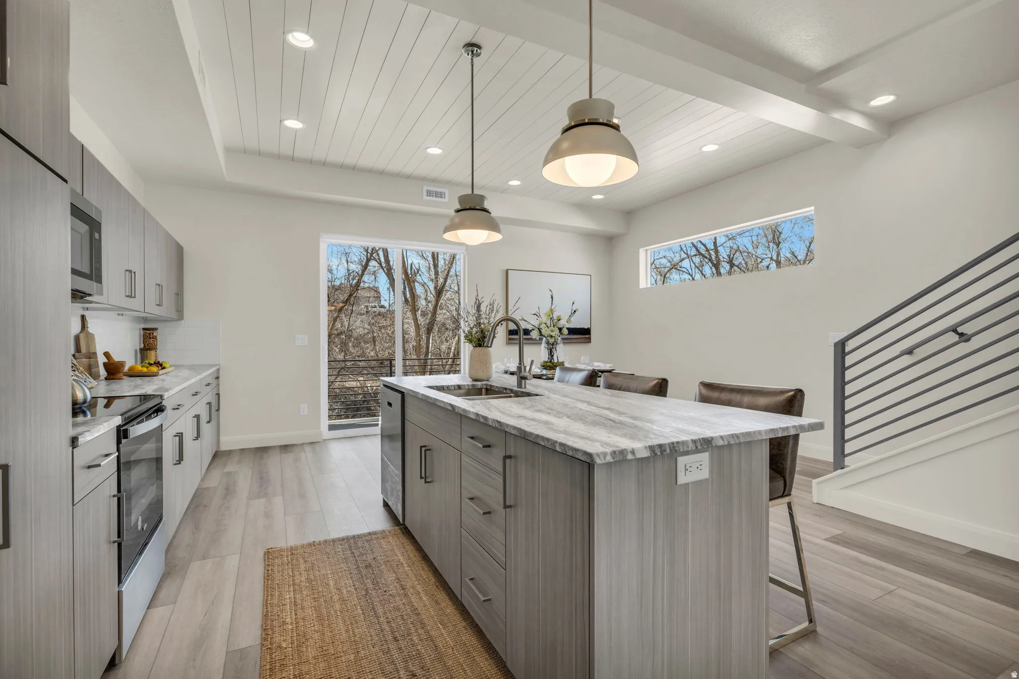 Contemporary kitchen featuring a large island with integrated sink, light wood-finish flooring, and sleek grey cabinetry