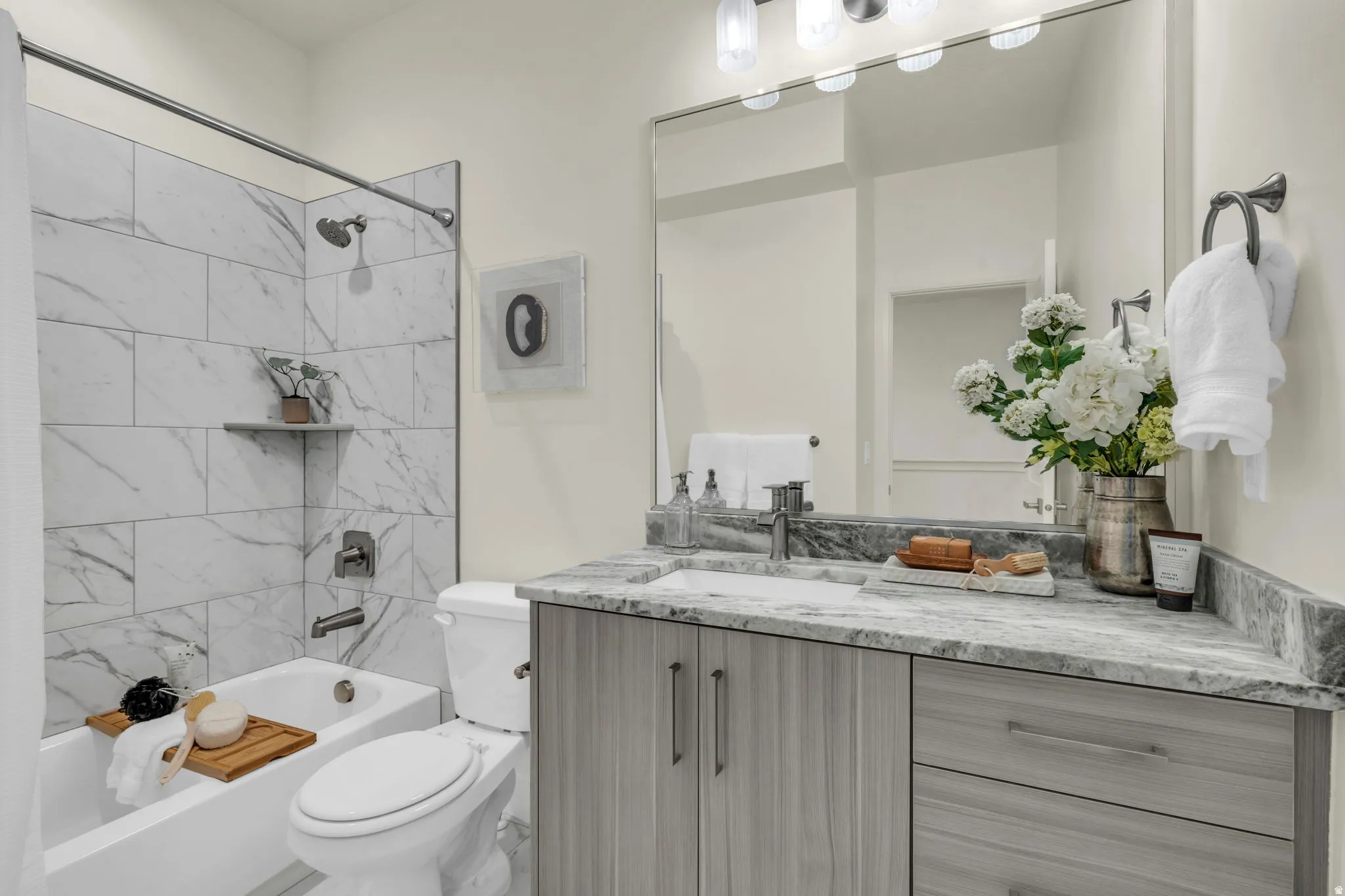 Full bathroom featuring a white tub with marble-look tile surround, a built-in corner shelf, and brushed nickel fixtures