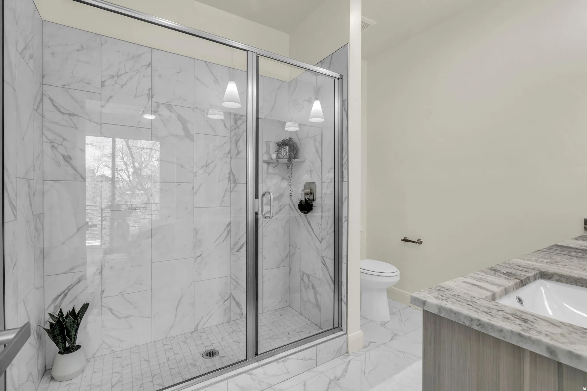 Walk-in shower with clear glass enclosure, white marble-look tile walls, and a tiled shower pan