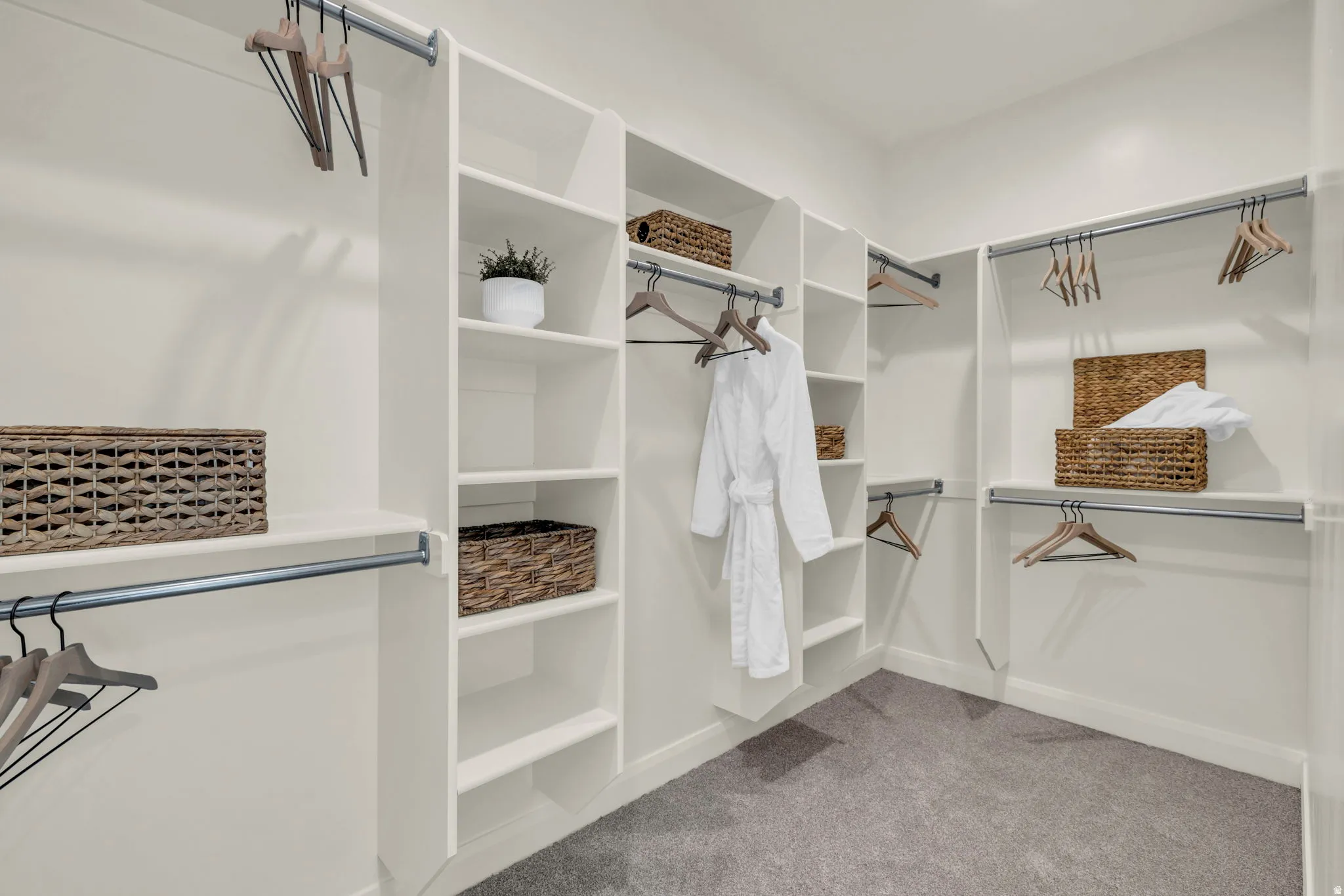 Walk-in closet featuring built-in shelving, multiple hanging rods, white cabinetry, neutral wall color, and grey carpet flooring