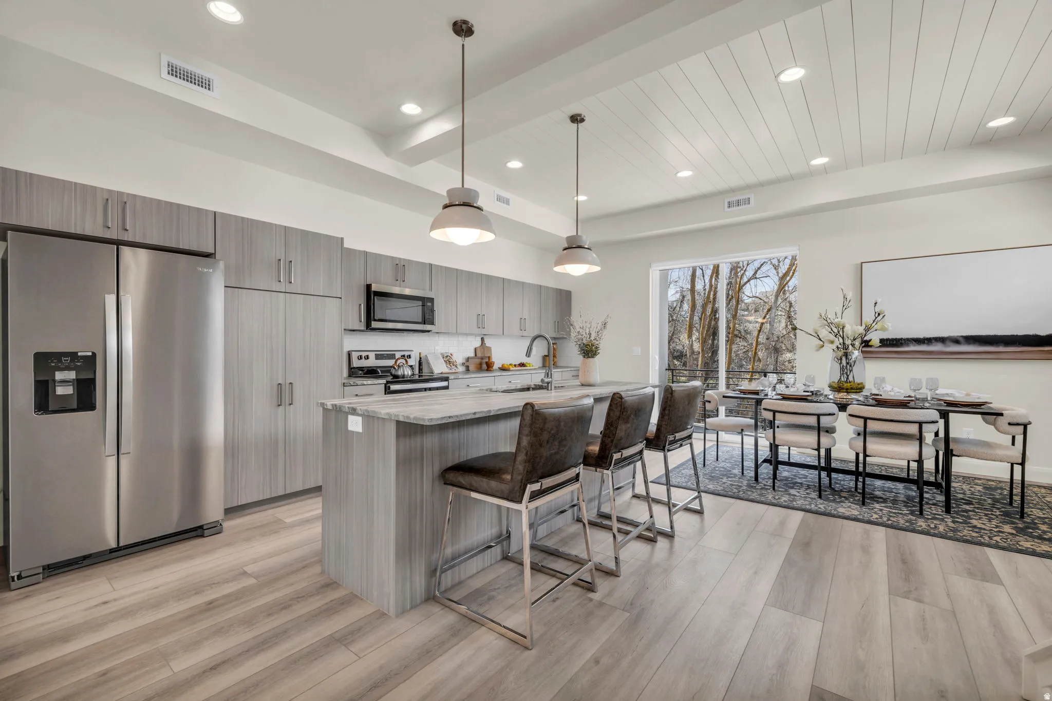 Open-concept kitchen and dining area featuring light wood-finish flooring, a kitchen island with seating, stainless steel appliances, modern cabinetry, and a shiplap ceiling