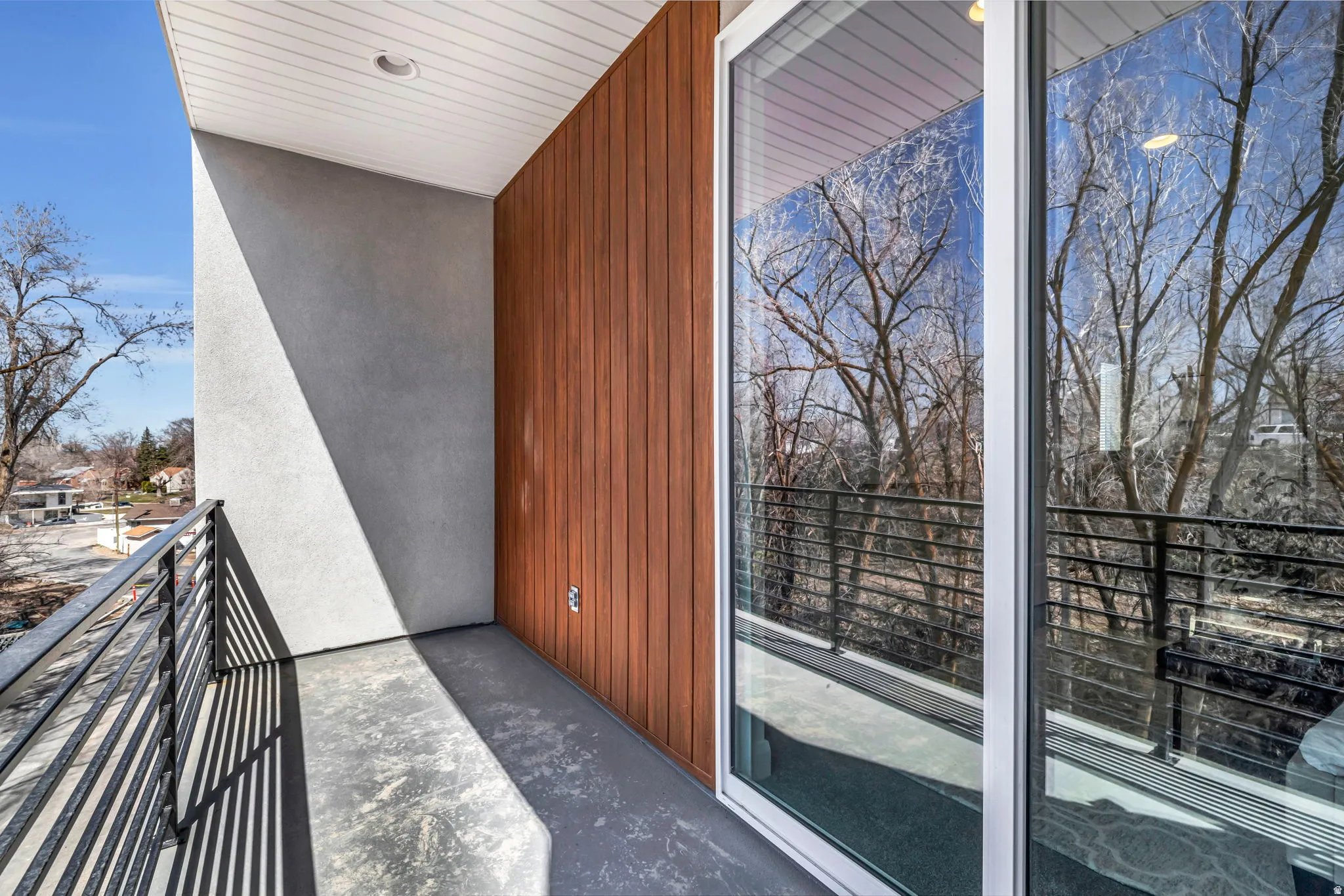Private outdoor balcony featuring a concrete floor, horizontal metal railings, and a wood-panel accent wall