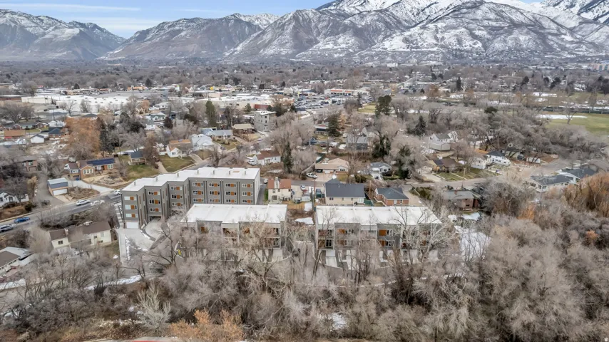 Modern multi-story residential buildings featuring balconies and gray facades, situated within a developed area with extensive tree cover