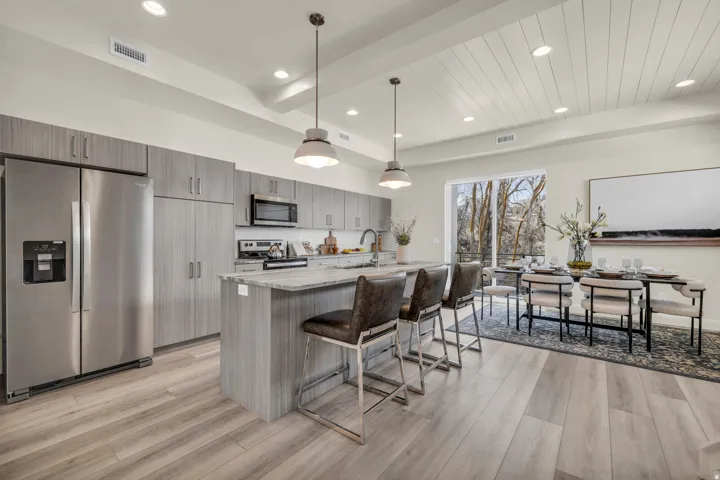 Open-concept kitchen and dining area featuring light wood-finish flooring, a kitchen island with seating, stainless steel appliances, modern cabinetry, and a shiplap ceiling