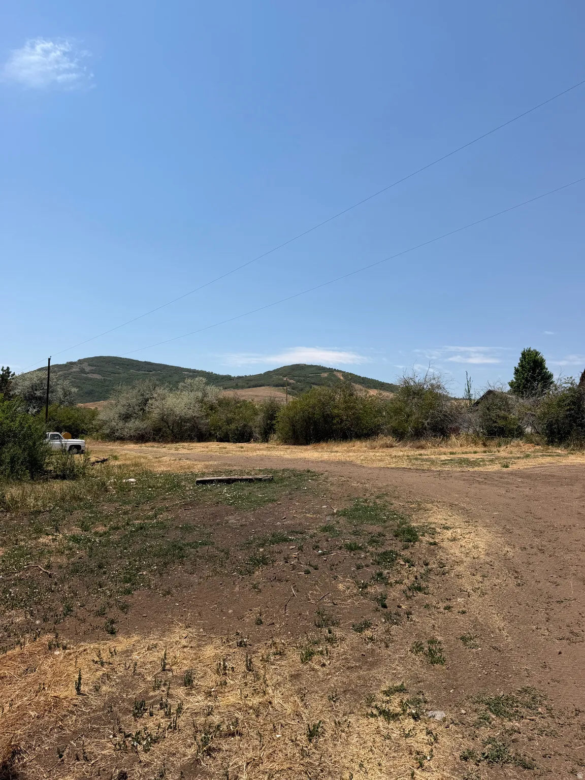 Expansive lot featuring a dirt and dry grass ground cover, surrounded by natural brush and distant hills