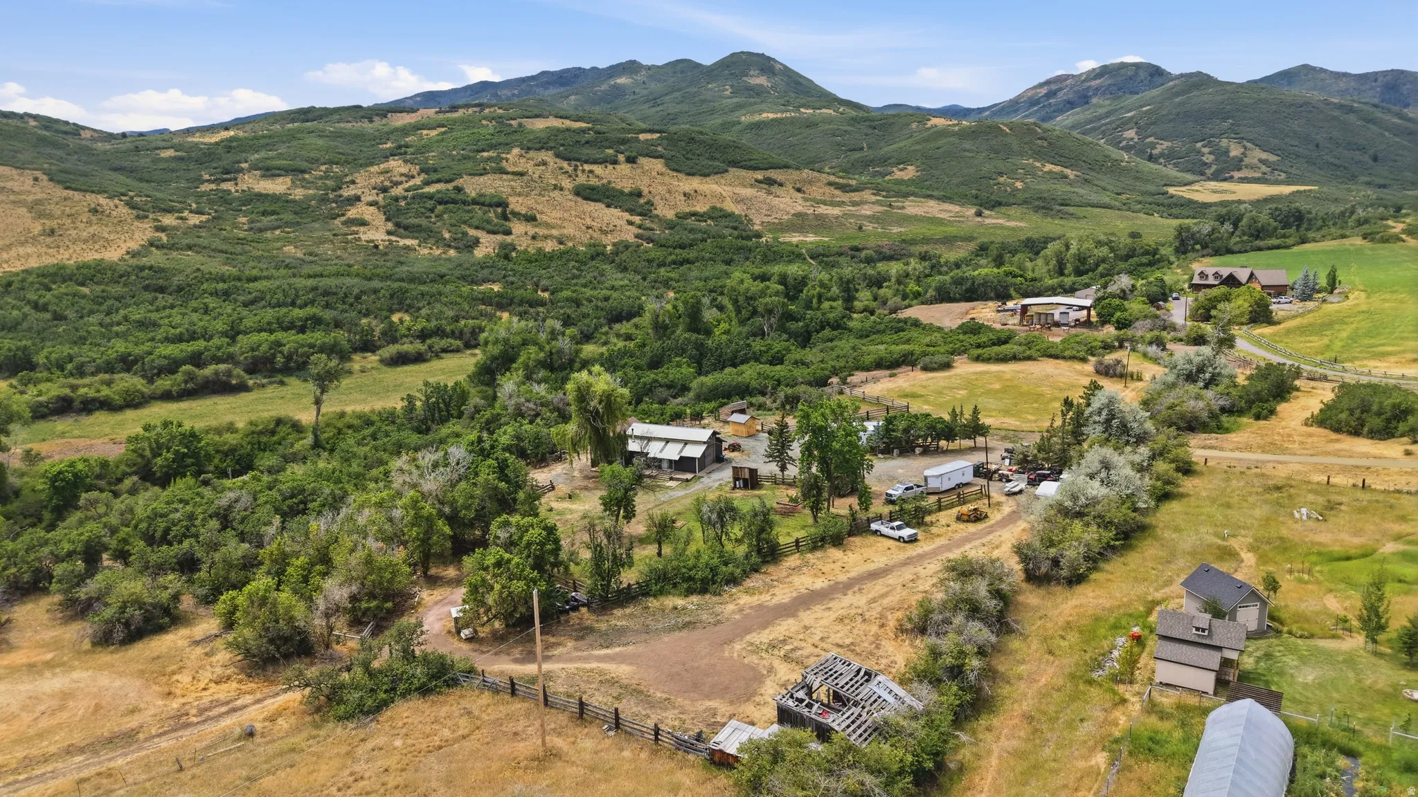 Expansive property featuring verdant hillsides, mature tree lines, multiple structures, and open fields, all surrounded by mountainous terrain