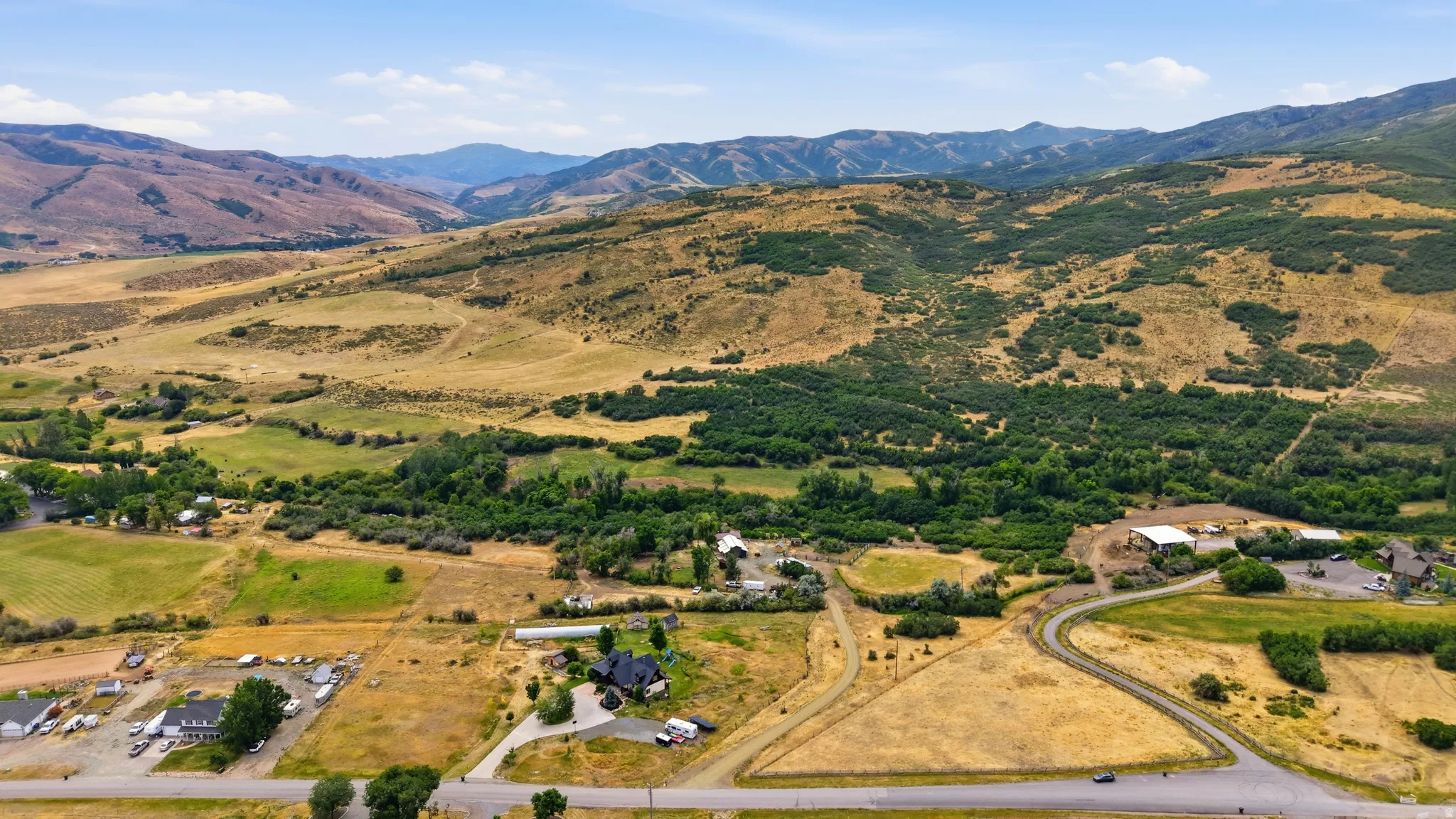 Expansive rural property featuring a winding paved road, a cluster of buildings with white roofs, and a separate large residence with a black roof