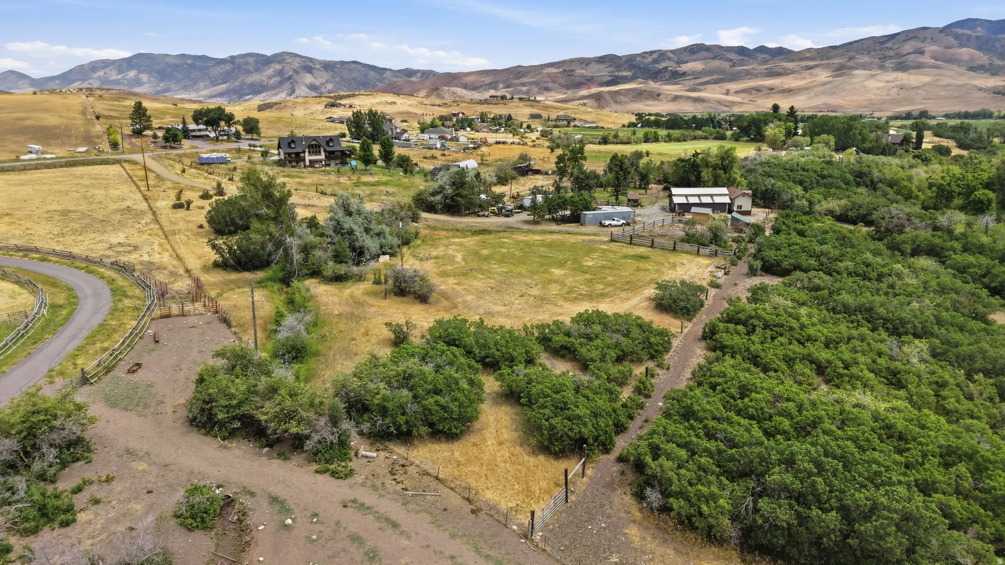 Expansive rural landscape featuring a winding paved road, diverse vegetation, and distant mountain ranges