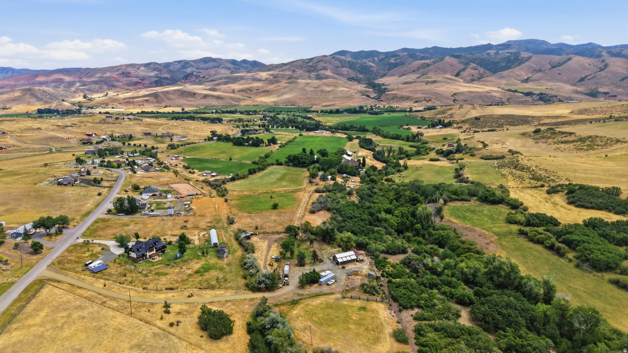 Expansive rural landscape featuring a mix of cultivated green fields and dry grasslands, surrounded by distant mountains