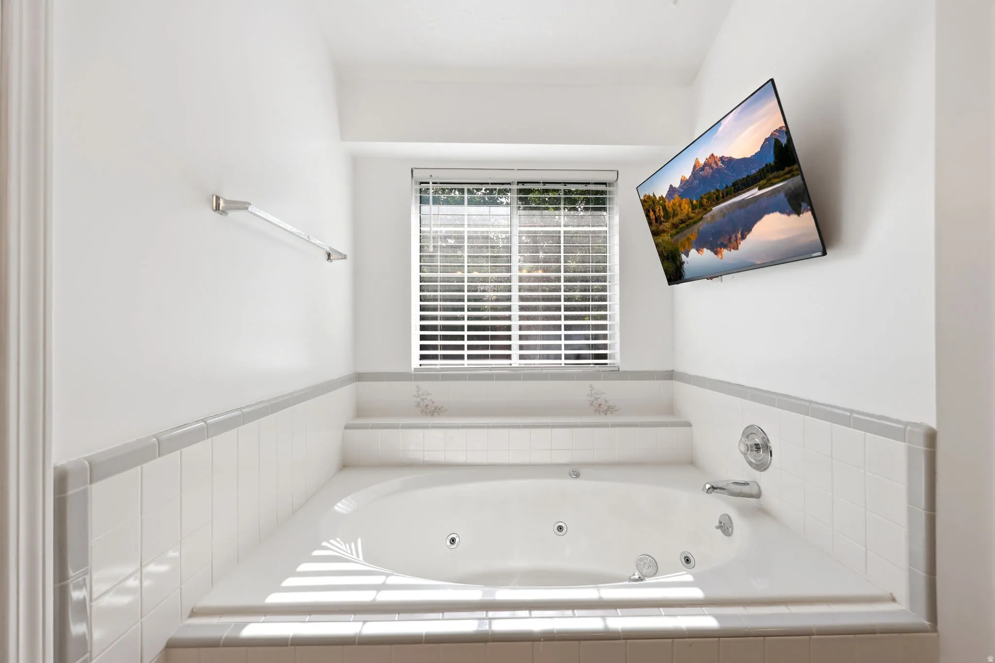 Soaking tub with jets, white tile surround, privacy blinds, and chrome fixtures
