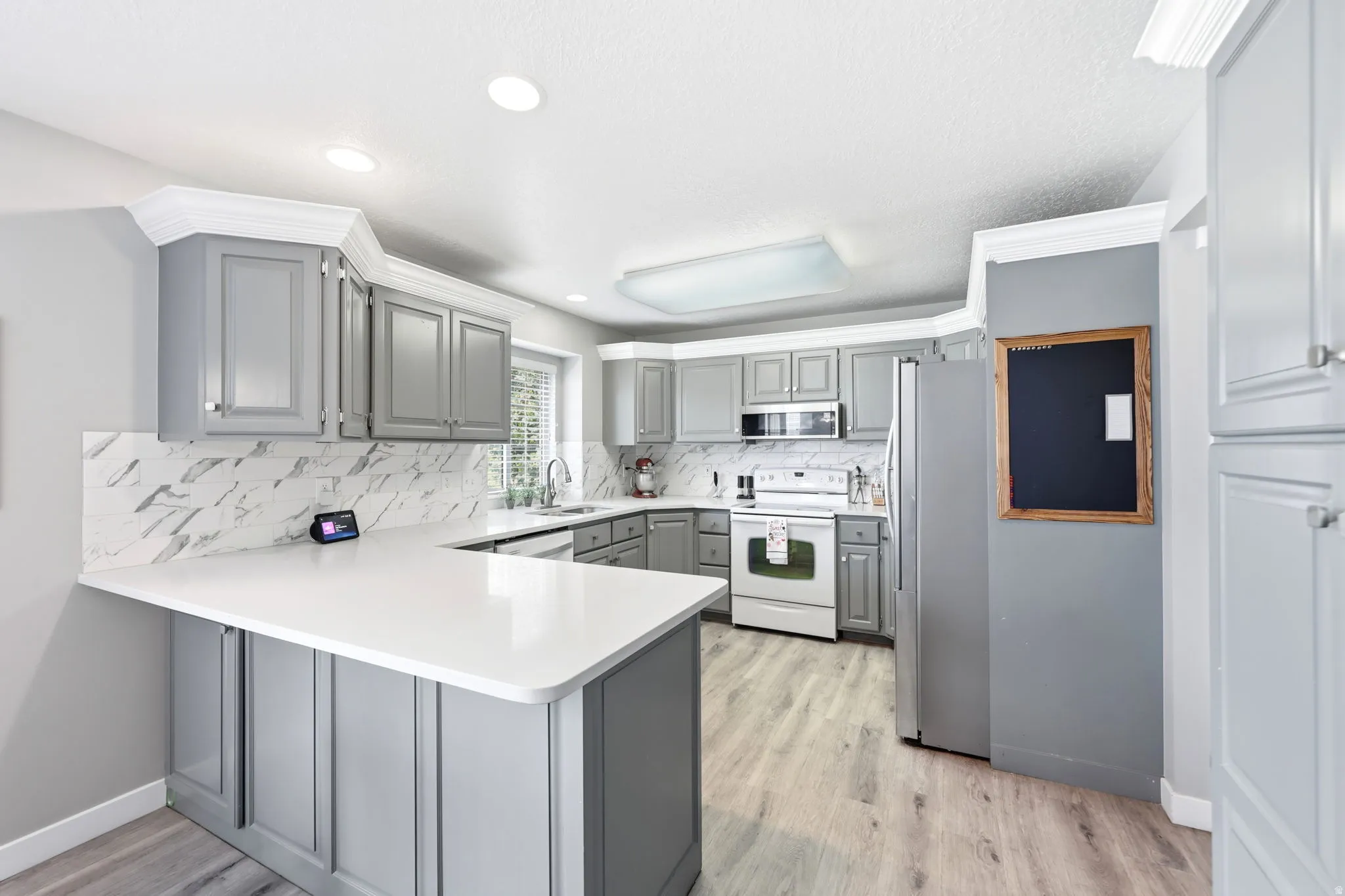 Kitchen featuring gray cabinetry, white countertops, marble-look tile backsplash, stainless steel appliances, and wood-finish flooring