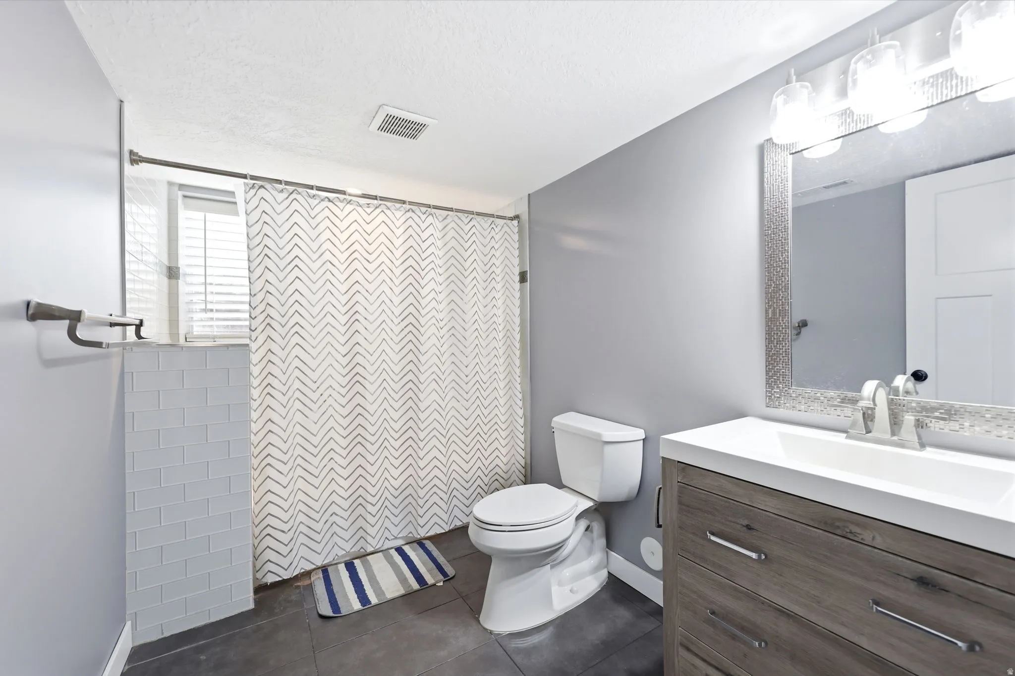 Modern bathroom featuring a contemporary vanity with a white countertop and integrated sink, a textured framed mirror, and a wall-mounted light fixture