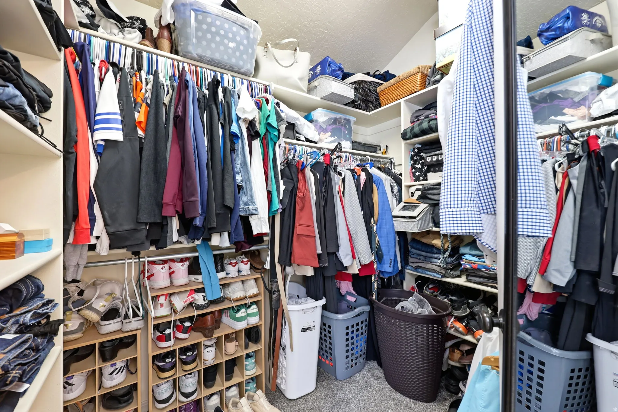 Walk-in closet featuring extensive built-in shelving, multiple hanging rods, dedicated shoe storage, and soft carpet flooring